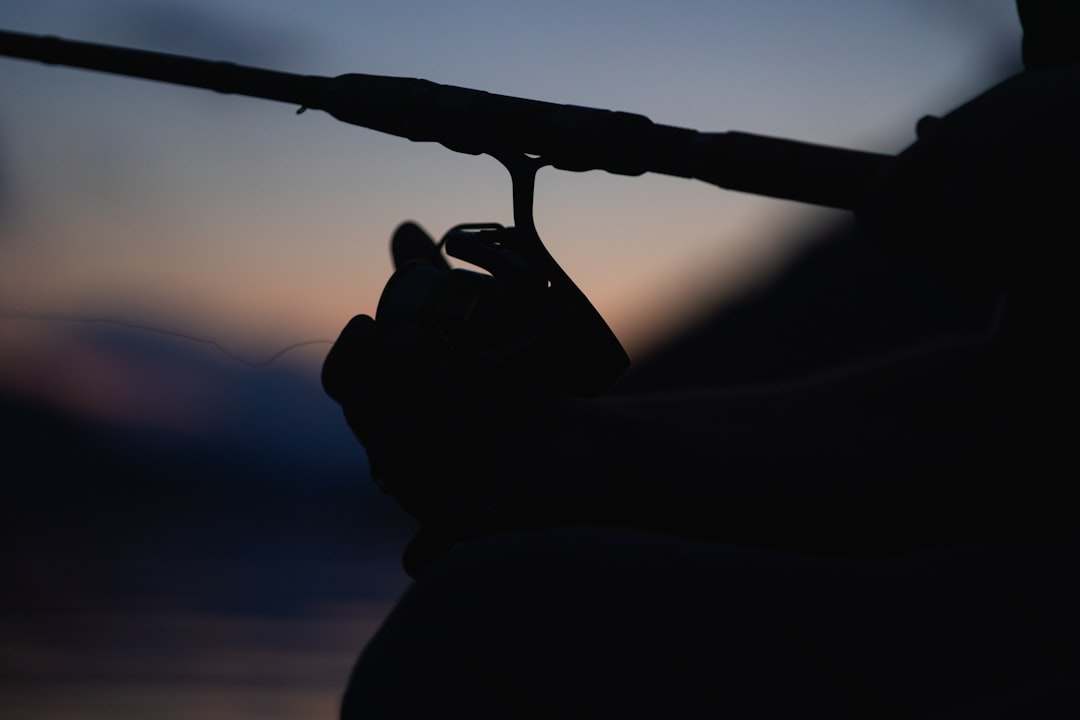 An angler casts a fishing line from the side of a boat on the open ocean during a dramatic sunrise, with golden light reflecting on the water.