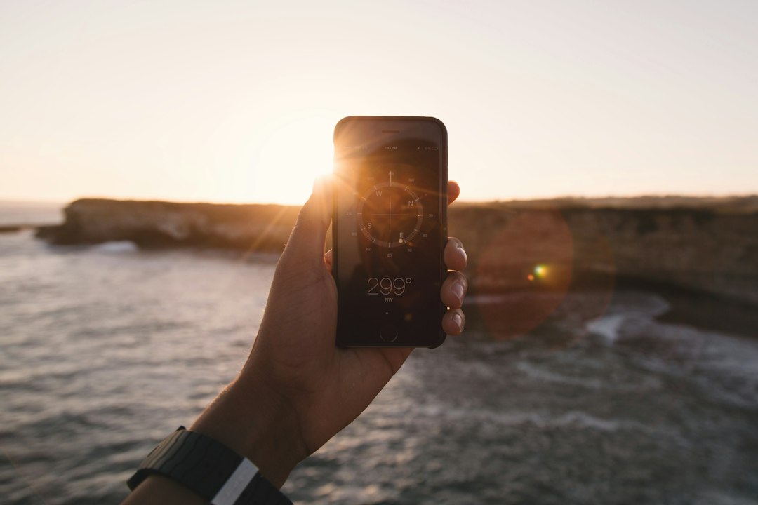 Close-up of a person's hand holding a smartphone displaying a map location, with the water of a marina in the background, symbolizing a customer finding a local charter.